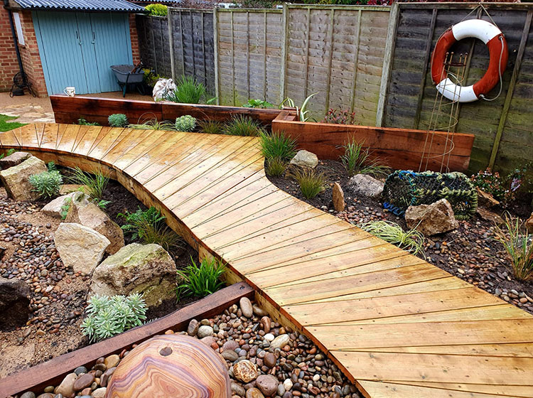 Close of of boardwalk style decking area with beach pebbles and rockery