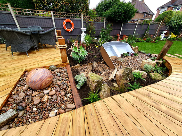 Close of of boardwalk style decking area with beach pebbles and rockery